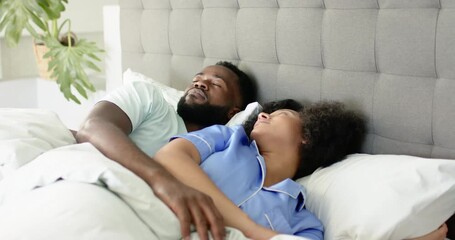 African American couple wearing pajamas spooning in bed shifting as man sitting up waking partner - Powered by Adobe