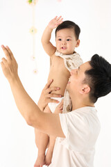 An 18-month-old Asian boy wrapped in a bath towel, standing with a superhero pose