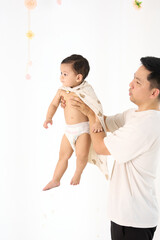 An 18-month-old Asian boy wrapped in a bath towel, standing with a superhero pose