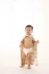 An 18-month-old Asian boy wrapped in a bath towel, walking with a superhero pose with an adult