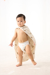 An 18-month-old Asian boy wrapped in a bath towel, standing with a superhero pose