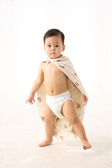 An 18-month-old Asian boy wrapped in a bath towel, walking with a superhero pose