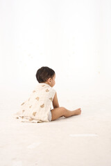 An 18-month-old Asian boy wrapped in a bath towel, sitting with a superhero pose
