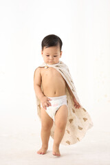 An 18-month-old Asian boy wrapped in a bath towel, walking with a superhero pose