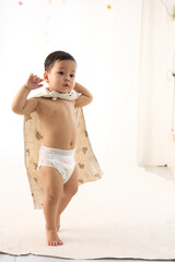 An 18-month-old Asian boy wrapped in a bath towel, standing with a superhero pose