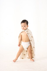 An 18-month-old Asian boy wrapped in a bath towel, standing with a superhero pose
