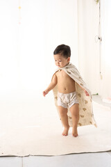 An 18-month-old Asian boy wrapped in a bath towel, walking with a superhero pose