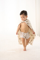 An 18-month-old Asian boy wrapped in a bath towel, standing with a superhero pose