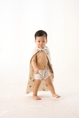 An 18-month-old Asian boy wrapped in a bath towel, walking with a superhero pose
