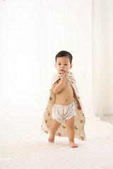 An 18-month-old Asian boy wrapped in a bath towel, standing with a superhero pose