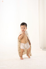 An 18-month-old Asian boy wrapped in a bath towel, walking with a superhero pose