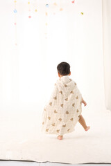 An 18-month-old Asian boy wrapped in a bath towel, walking with a superhero pose