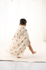 An 18-month-old Asian boy wrapped in a bath towel, walking with a superhero pose