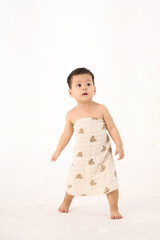 An 18-month-old Asian boy wrapped in a bath towel, walking with a superhero pose