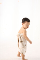 An 18-month-old Asian boy wrapped in a bath towel, standing with a superhero pose