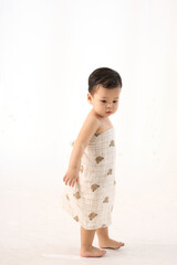 An 18-month-old Asian boy wrapped in a bath towel, walking with a superhero pose
