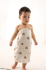 An 18-month-old Asian boy wrapped in a bath towel, walking with a superhero pose