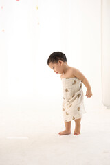 An 18-month-old Asian boy wrapped in a bath towel, walking with a superhero pose with an adult