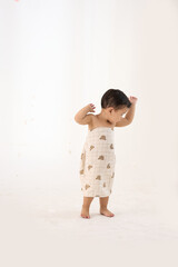 An 18-month-old Asian boy wrapped in a bath towel, standing with a superhero pose