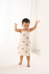 An 18-month-old Asian boy wrapped in a bath towel, standing with a superhero pose
