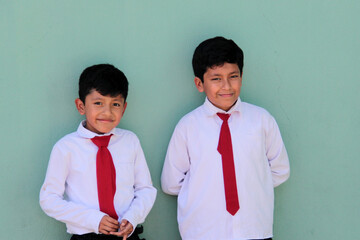 Two dark-skinned Latino male classmates dressed in uniform are excited and happy to be back in...