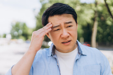 Asian man suffering from headache touching his forehead outdoors