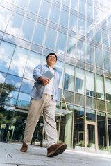 Asian businessman walking outside modern office building holding laptop
