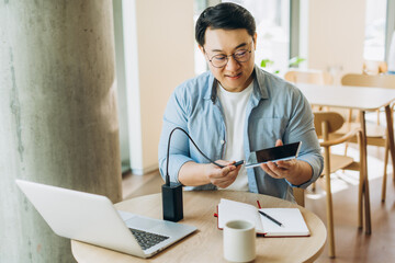 Asian freelancer connecting tablet to power bank in cafe