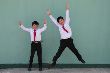 Two dark-skinned Latino male classmates dressed in uniform are excited and happy to be back in...
