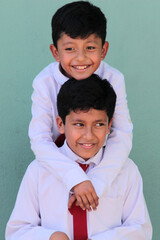 Two dark-skinned Latino male classmates dressed in uniform are excited and happy to be back in...