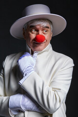 Close-up portrait of a clown. An elderly man in a white coat and hat.