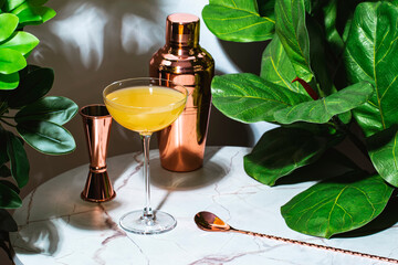 Yellow alcoholic cocktail drink with whiskey, liqueur and lemon juice with bar tools. Marble table...