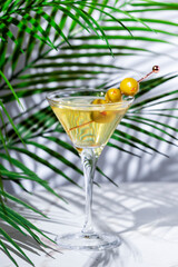 Dirty martini cocktail drink with gin or vodka, dry vermouth, olive brine and green olives. Marble table with palm leaves