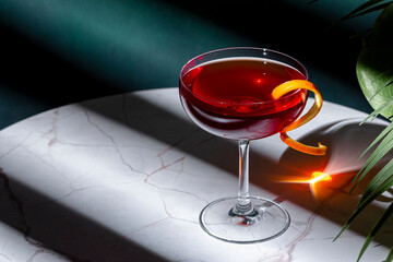 Red strong alcoholic cocktail drink with scotch whiskey, liqueur and orange twist on green...