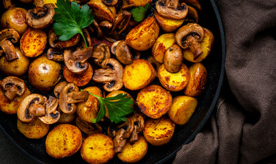 Baked golden potatoes with mushrooms in frying pan. Black background, top view