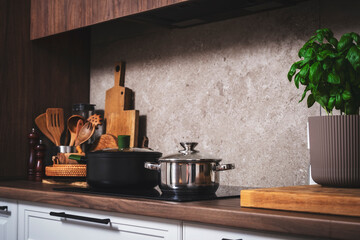Cozy modern kitchen with cooking utensils, pots, cutting boards on wooden countertop with porcelain...