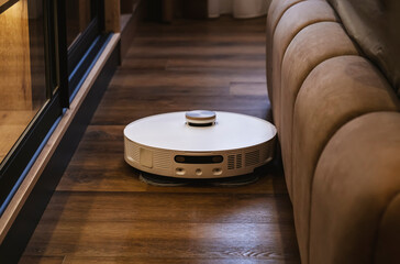 White robot vacuum cleaner mopping floors and vacuuming while cleaning in beautiful modern bedroom