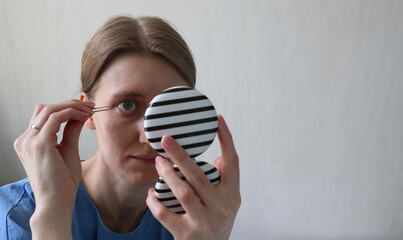 Woman takes care of her eyebrows. Plucks her eyebrows with tweezers. Looks in a pocket, round...