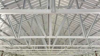 A symmetrical view of a metal roof structure featuring interconnected steel beams and trusses. The...