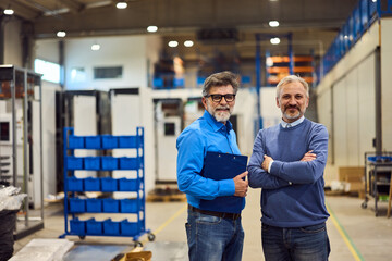 Two Professional Men Smiling Confidently in a Modern Industrial Warehouse Setting