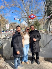 Trio Posing at Subway Entrance: Friends stand together beneath a metro sign, bathed in daylight and...