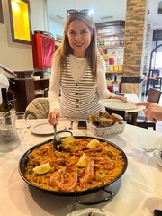 Delighted Dining Moment: A smiling individual presents a delectable seafood paella at a table,...