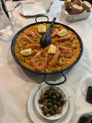 Exquisite Paella Feast: A vibrant paella dish, brimming with succulent shrimp and zesty lemon wedges, served alongside olives and crusty bread, offering a tantalizing culinary experience.