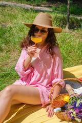 Woman enjoying a picnic outdoors with food and flowers in the sun. She enjoys a refreshing drink...