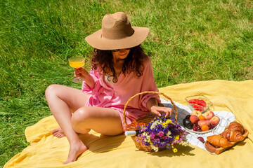 Woman enjoying a picnic outdoors with food and flowers in the sun. She enjoys a refreshing drink...
