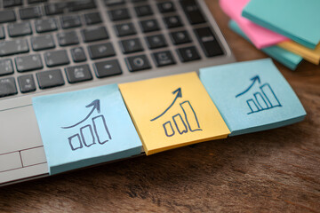 Business growth concept with sticky notes showing upward trending graphs on laptop keyboard with a...