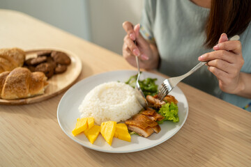 Close up of woman eating chicken teriyaki with rice in kitchen at home.