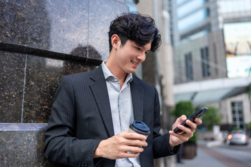 Asian young businessman chatting on smartphone while standing in city. 
