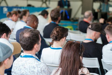 Group of attendees seated during seminar focused on lecture with blue lanyards visible