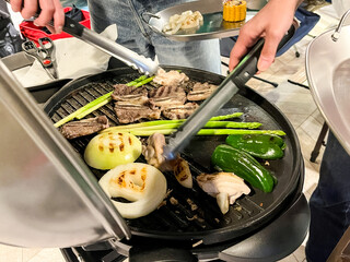 トングを使いバーベキューで肉と野菜を焼く人々